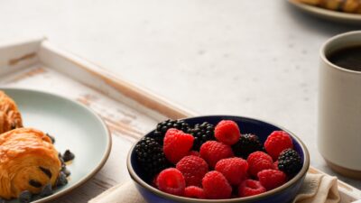 A cup of black coffee with coffee beans, berries and nuts on a bright table, representing coffee within a balanced anti-inflammatory diet.