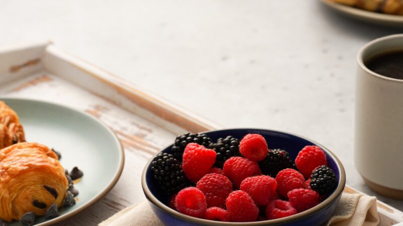 A cup of black coffee with coffee beans, berries and nuts on a bright table, representing coffee within a balanced anti-inflammatory diet.