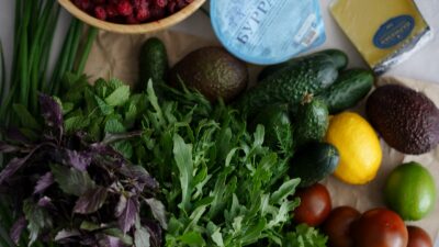 Anti-inflammatory grocery staples including vegetables, berries, whole grains, beans, salmon, nuts, seeds, olive oil and plain yogurt arranged on a bright counter.