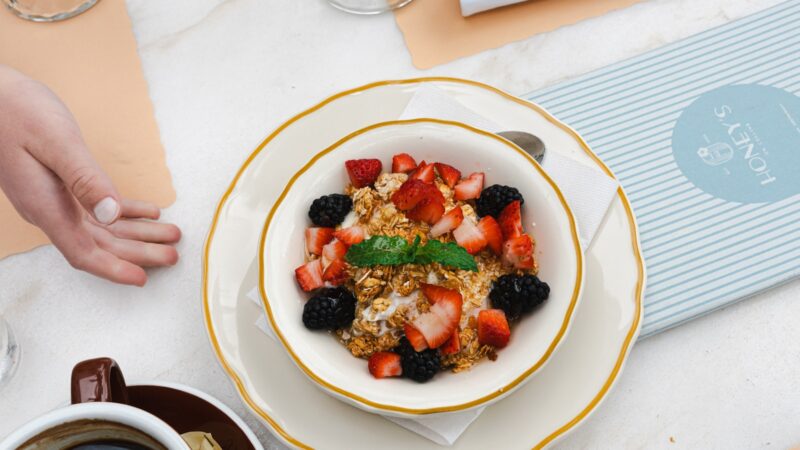 Berry oatmeal, avocado egg toast with tomatoes, and yogurt with berries and seeds arranged on a bright breakfast table.