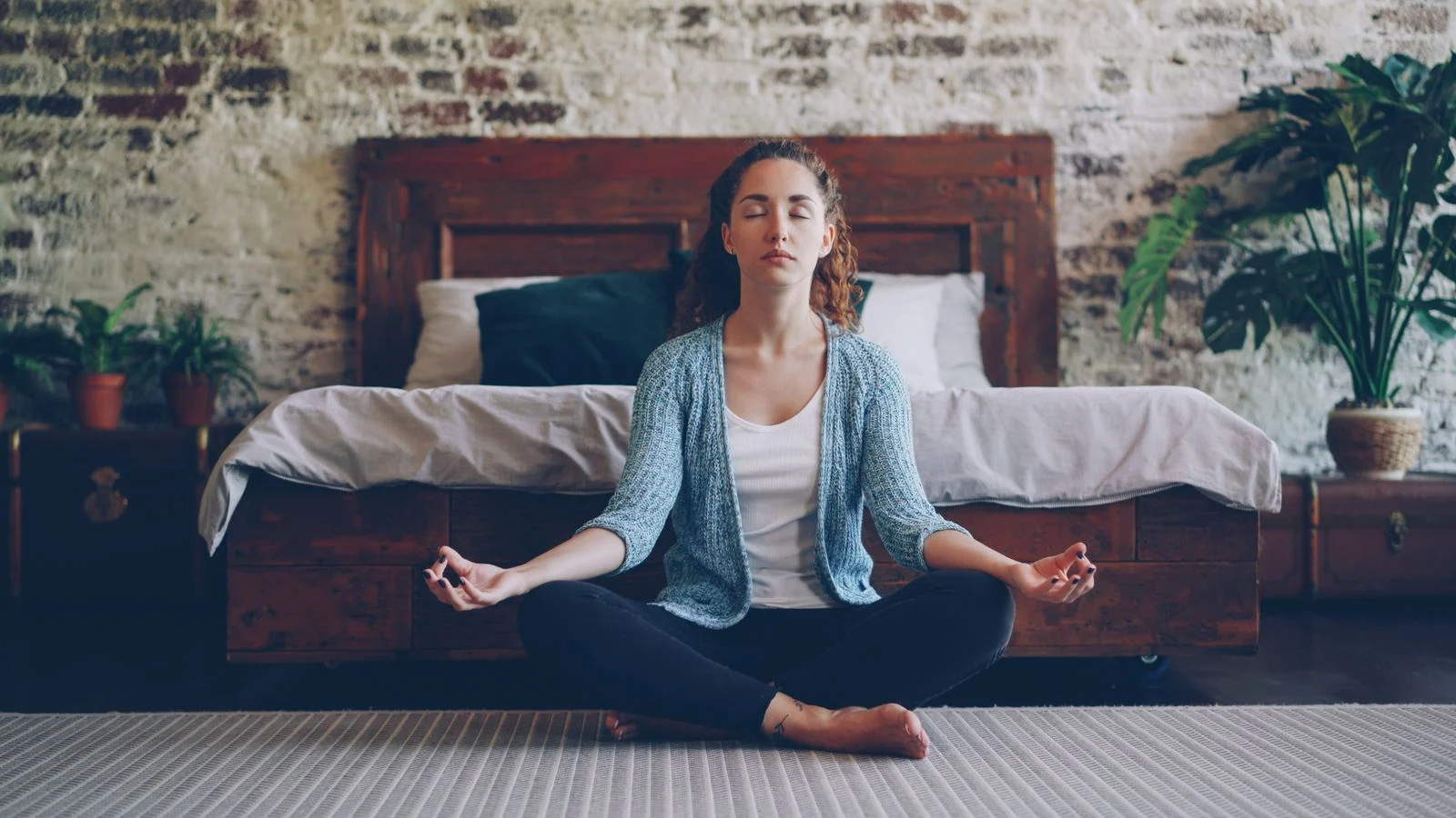 Adult practicing calm breathing and meditation beside a bed as part of a bedtime relaxation routine.