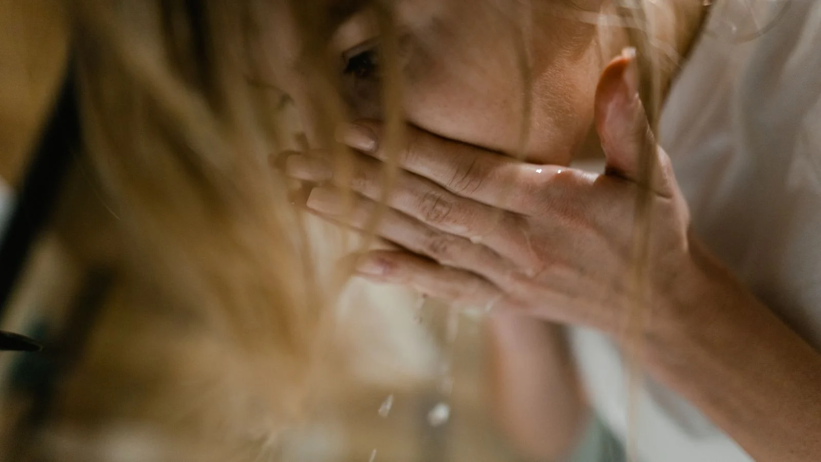 Adult gently refreshing the face with cool water at a sink, illustrating mild facial cooling.